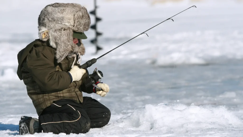 A person ice fishing wearing bulky clothes