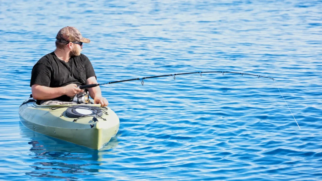 A person fishing from the kayak wearing a hat