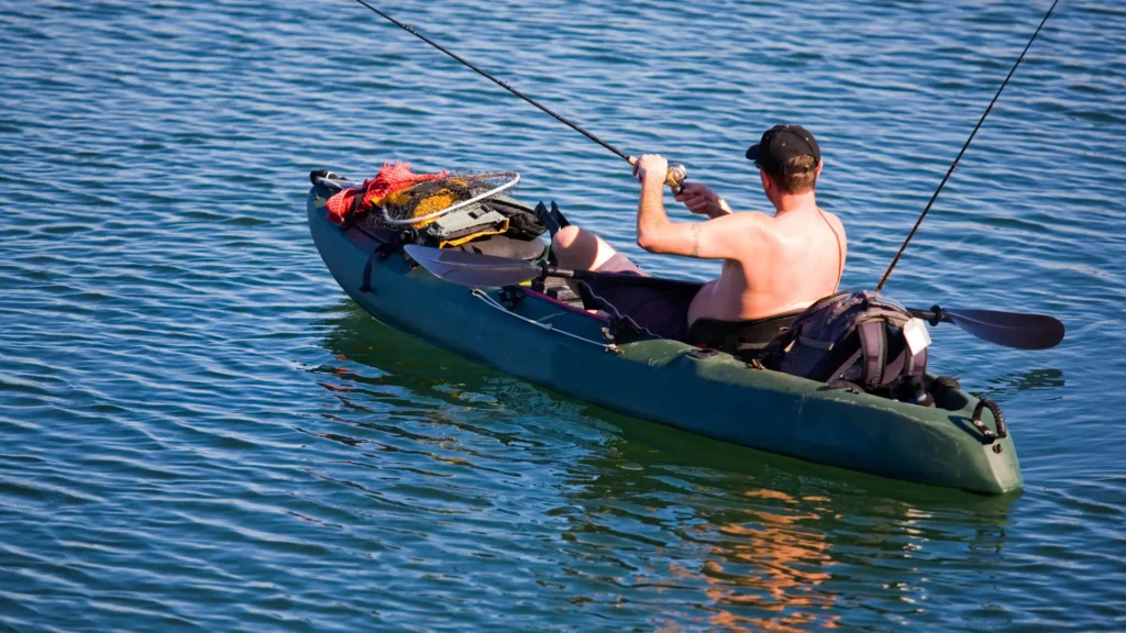 A person fishing from the kayak wearing no shirt