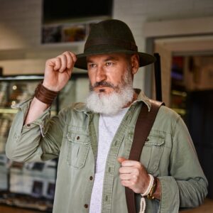 bearded male hunter tries on hat in gun store e1628080948327